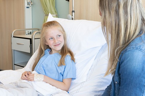 Meisje in ziekenhuisbed kijkt lachend haar moeder aan