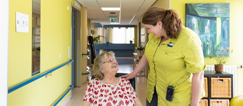 Mevrouw in rolstoel kijkt medewerker Revalidatie lachend aan