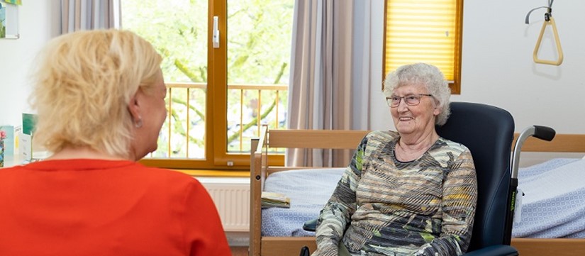 Mevrouw in rolstoel op haar kamer in gesprek met Rivas medewerker